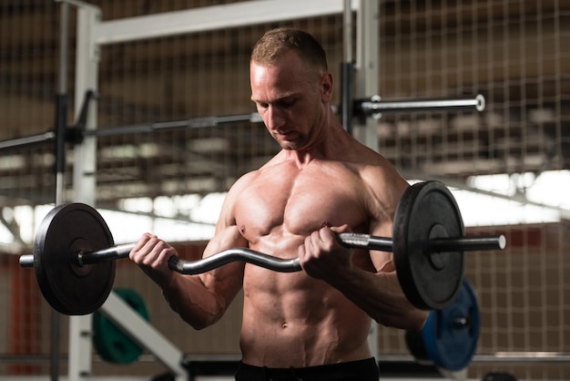 Homme dans la salle de gym exerçant des biceps avec des haltères