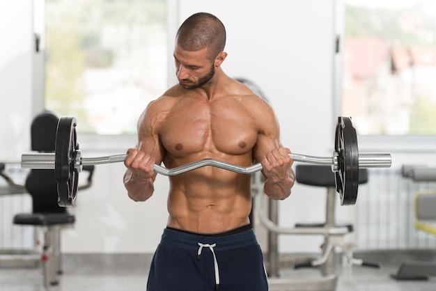 Homme dans la salle de gym exerçant des biceps avec des haltères