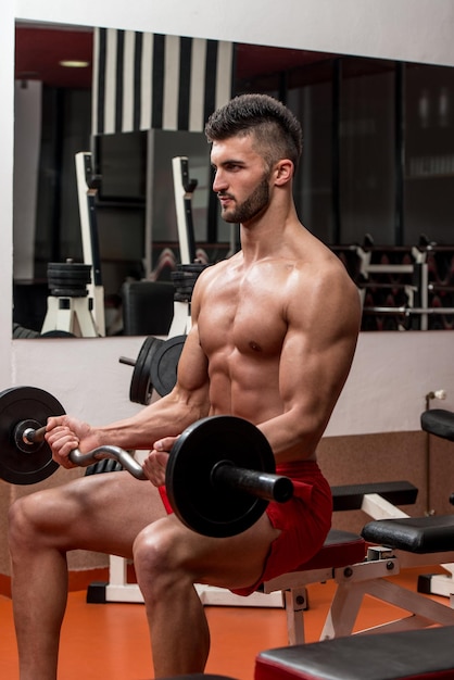 Homme dans la salle de gym exerçant des biceps avec des haltères