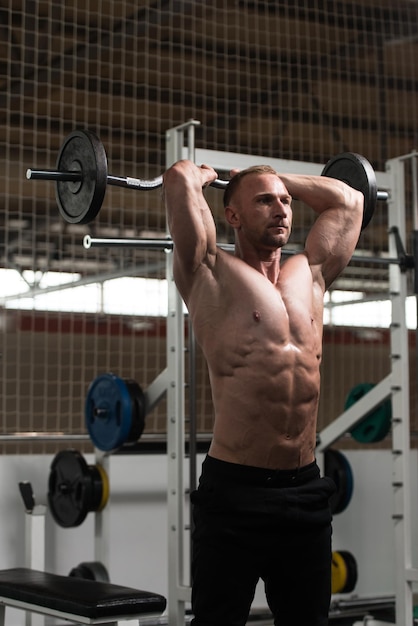 Homme dans la salle de gym exerçant des triceps avec des haltères