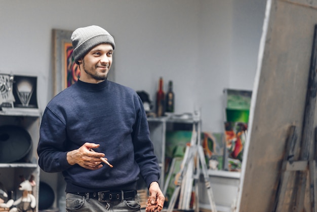 Homme dans un studio d'art avec un pinceau dans ses mains, regardant la toile et souriant