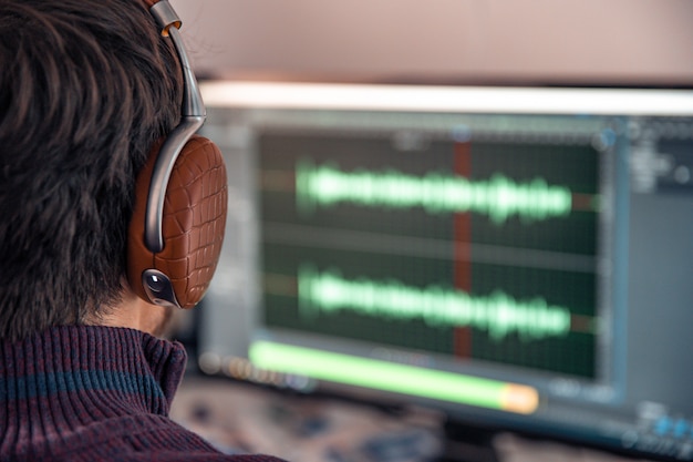 Photo l'homme dans le studio photo enregistre et modifie le chant, la voix et la musique à des fins commerciales. fonctionne dans un éditeur audio sur un ordinateur avec casque