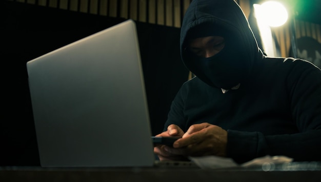 homme dans un sweat à capuche tenant de l'argent et utilisant un ordinateur portable creusant dans les données financières concept de vol Internet