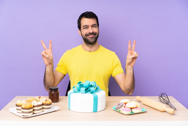 Homme dans une table avec un gros gâteau montrant le signe de la victoire à deux mains