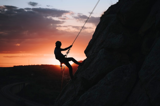 Homme dans la trentaine escaladant une montagne au coucher du soleil