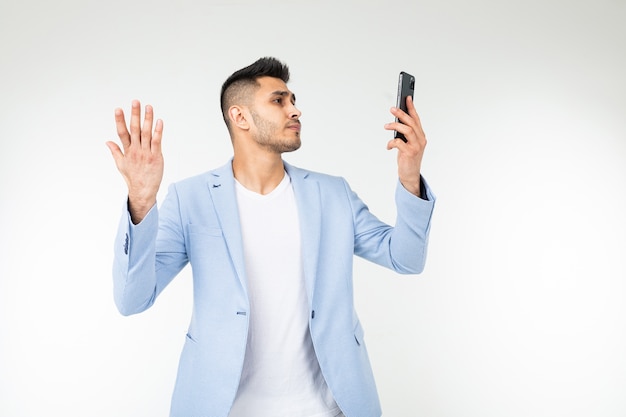 L'homme dans une veste bleue tente d'attraper la communication mobile sur un smartphone sur un fond blanc.