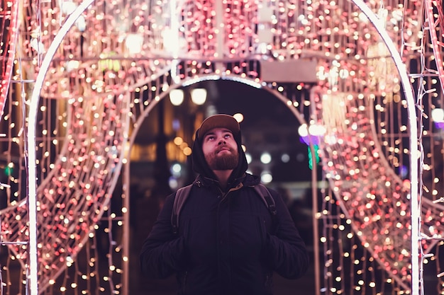 L'homme dans une veste se tient dans la ville de nuit sur le fond de l'éclairage de la ville