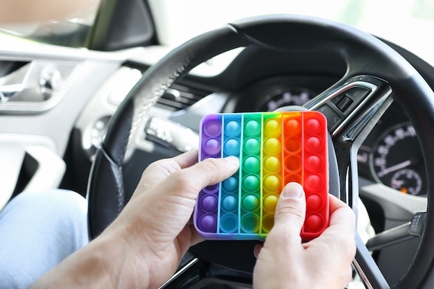 Un homme dans une voiture tient un simple jouet à fossettes aux couleurs de l'arc-en-ciel