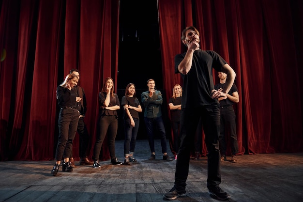 Homme debout contre des personnes Groupe d'acteurs vêtus de vêtements de couleur sombre en répétition au théâtre