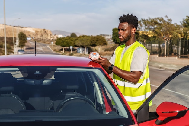 Un homme debout à côté d'une voiture rouge plaçant un feu d'urgence le long de la route dans un parking