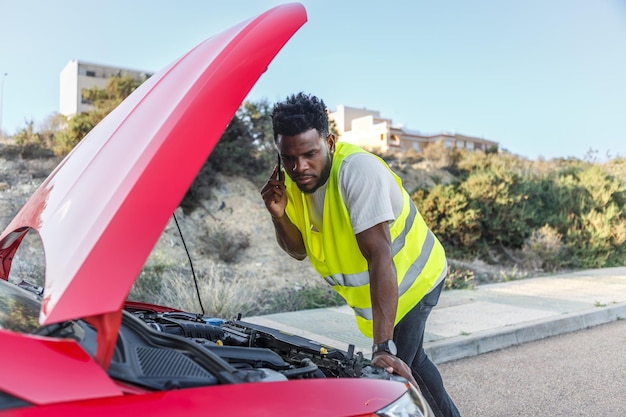 Un homme debout à côté d'une voiture rouge qui parle au téléphone portable