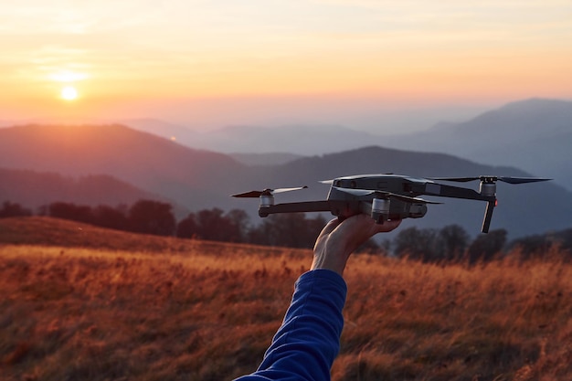 Homme debout dans le champ d'automne et tient un drone à la main Beau lever de soleil Paysage majestueux de montagnes au loin