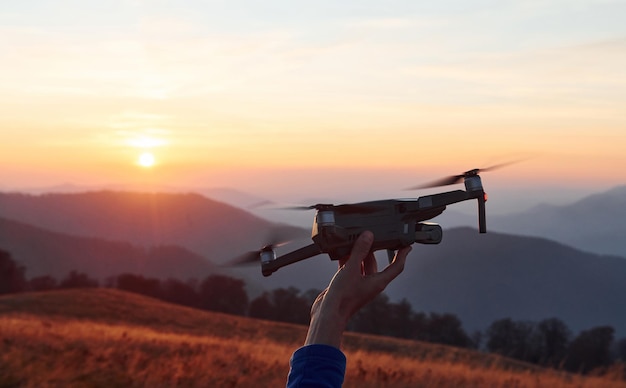 Homme debout dans le champ d'automne et tient un drone à la main Beau lever de soleil Paysage majestueux de montagnes au loin