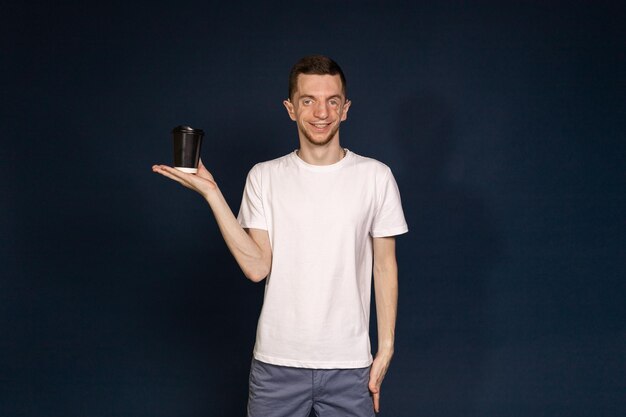 Un homme debout dans un fond bleu tenant un café à la main