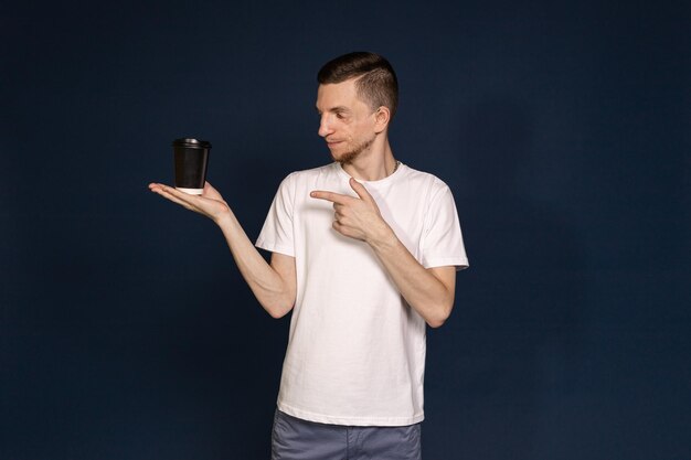 Un homme debout dans un fond bleu tenant un café à la main