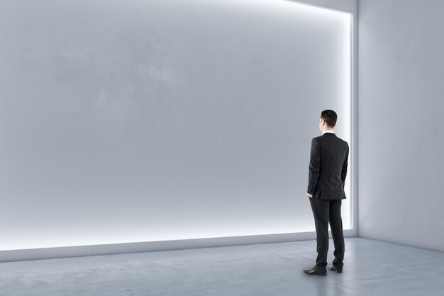 Homme debout dans un hall d'exposition moderne à l'intérieur avec un mur blanc éclairé et un sol en béton Concept de galerie