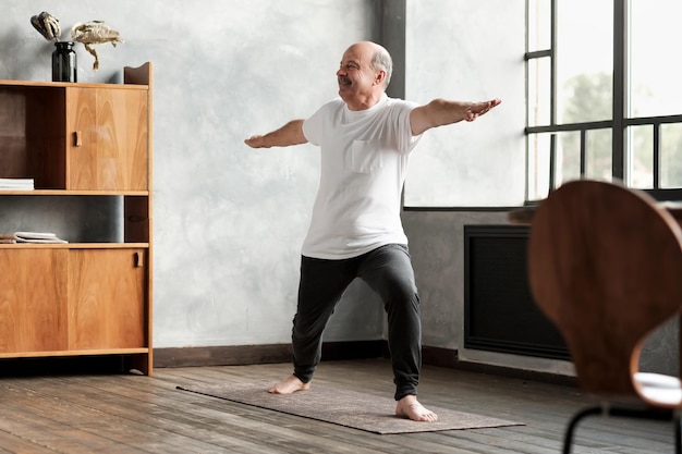 Homme debout dans la pose de yoga du guerrier deux pratiquant dans le salon