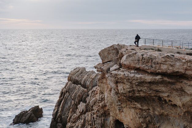 Homme debout sur une falaise et profitant de la vue panoramique sur le coucher du soleil