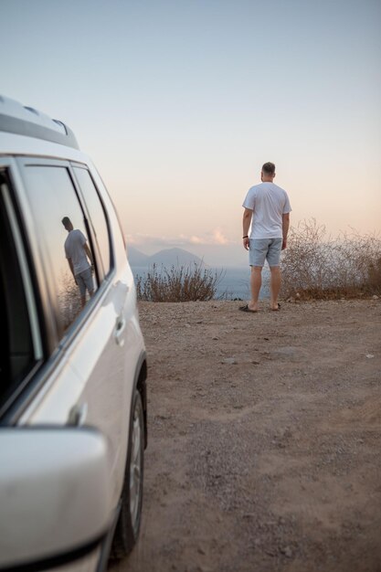 Homme debout à la falaise à la recherche sur le paysage de la mer voiture garée