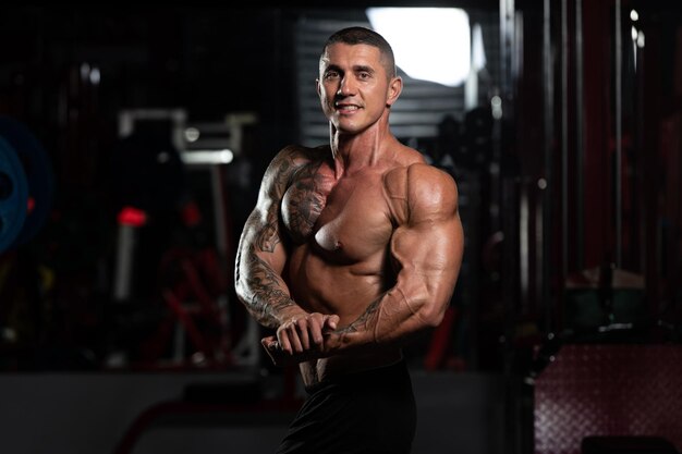 Homme debout fort dans la salle de sport et muscles de la flexion Modèle de forme physique de bodybuilder athlétique musclé posant après les exercices