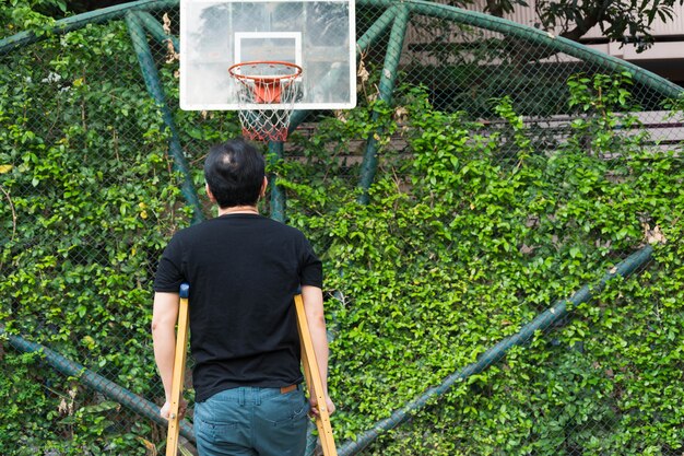 homme debout avec une jambe cassée dans un plâtre en utilisant des béquilles au terrain de basket