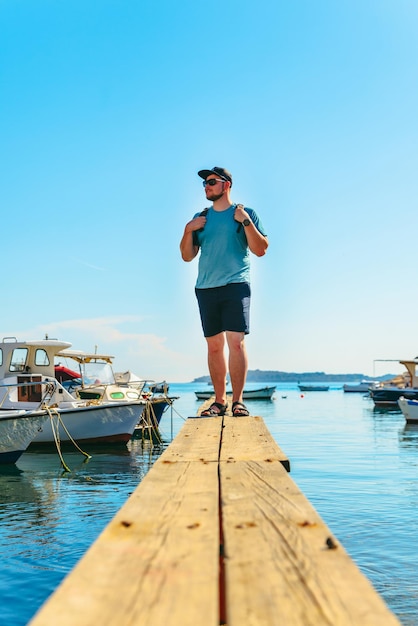 Homme debout sur une jetée en bois au quai des bateaux à l'heure d'été de la baie de la mer