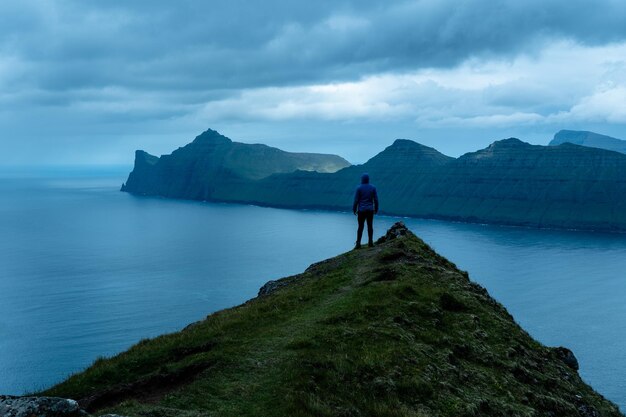 Un homme debout sur une montagne surplombant la mer et les montagnes des îles Féroé