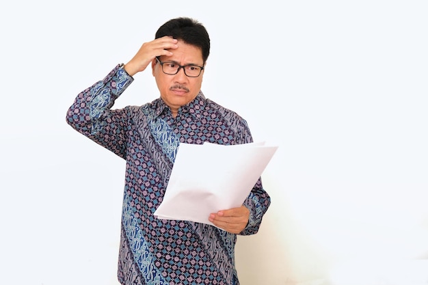 Photo un homme debout portant des vêtements formels de batik regardant stressé le papier dans ses mains