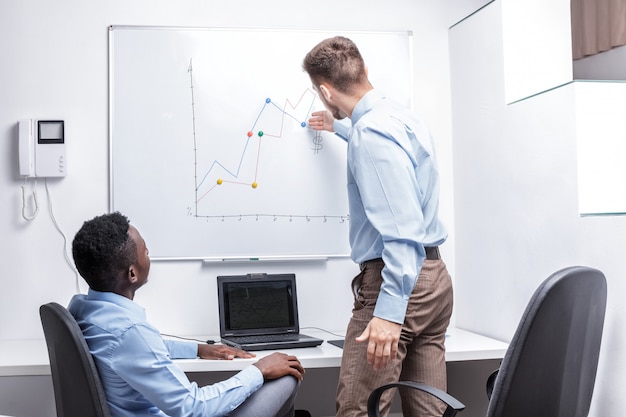 Homme debout près de tableau blanc et pointant sur le graphique