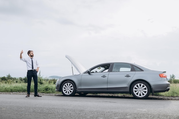 Homme debout près d'une voiture de dépannage et gesticulant avec la main