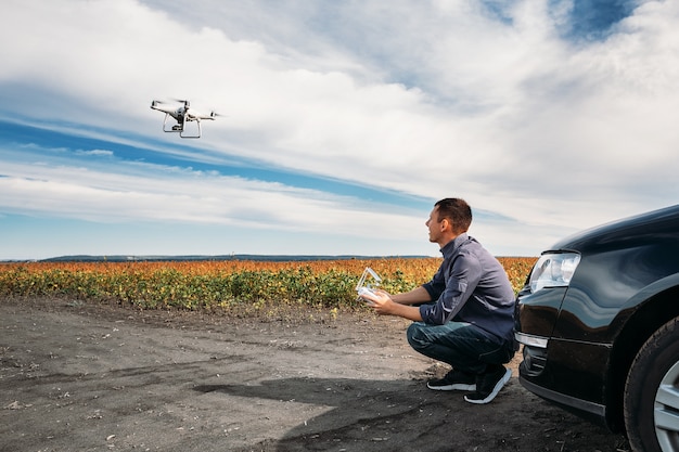 Un homme debout près de la voiture lance un drone. vol de drone dans le champ jaune