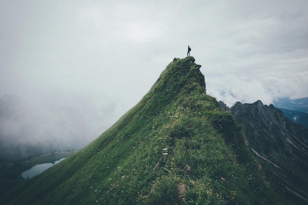 Un homme debout sur le sommet d'une montagne contre un ciel nuageux
