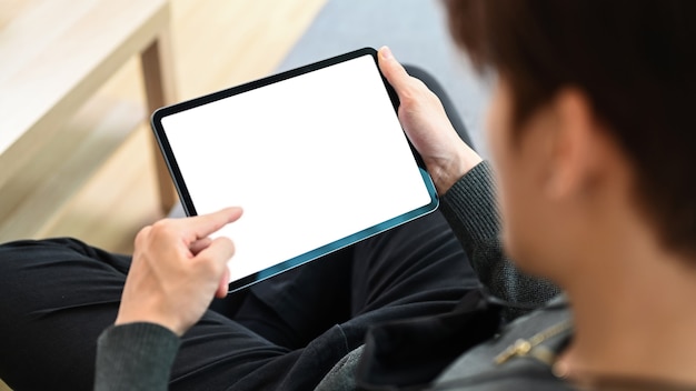 Homme décontracté assis sur un canapé avec les jambes croisées et à l'aide de tablette numérique.