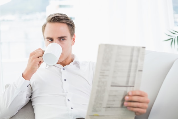 Homme décontracté, boire du café en lisant le journal sur le canapé