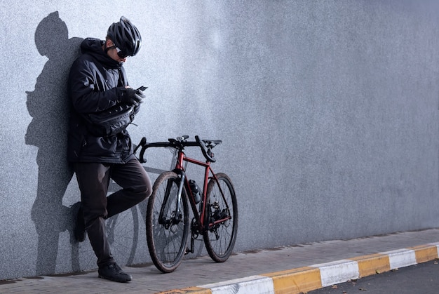 Homme décontracté se tient près d'un mur de béton gris avec un vélo et regarde le téléphone. Style urbain.
