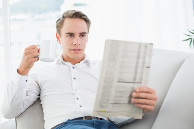 Homme décontracté avec une tasse de café en lisant un journal sur le canapé