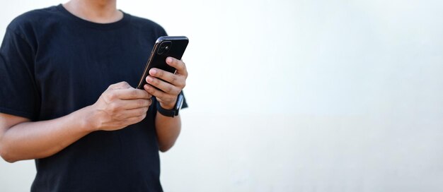 Homme décontracté utilisant un téléphone intelligent debout contre un mur blanc