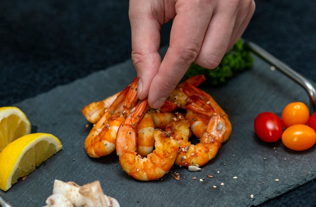 L'homme décore un plat de crevettes frites avec des légumes sur un plateau en pierre