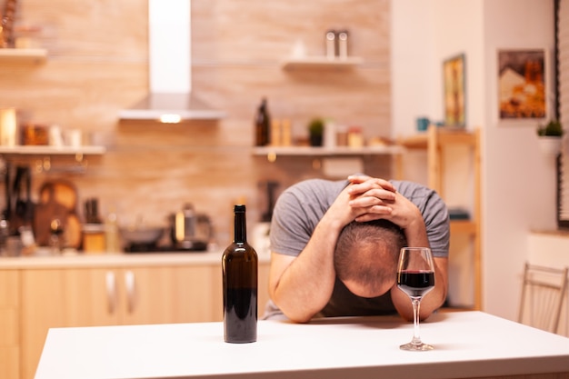 Homme déprimé ayant des maux de tête après l'abus d'alcool dans la cuisine. Maladie de la personne malheureuse et anxiété se sentant épuisée par des problèmes d'alcoolisme.