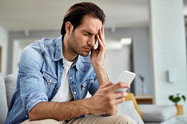 Homme désemparé ayant mal à la tête après avoir lu de mauvaises nouvelles sur un téléphone portable