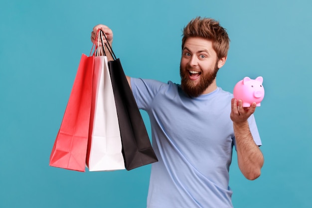 L'homme détient des sacs à provisions et une tirelire en espèces pour acheter des achats exprimant des émotions positives