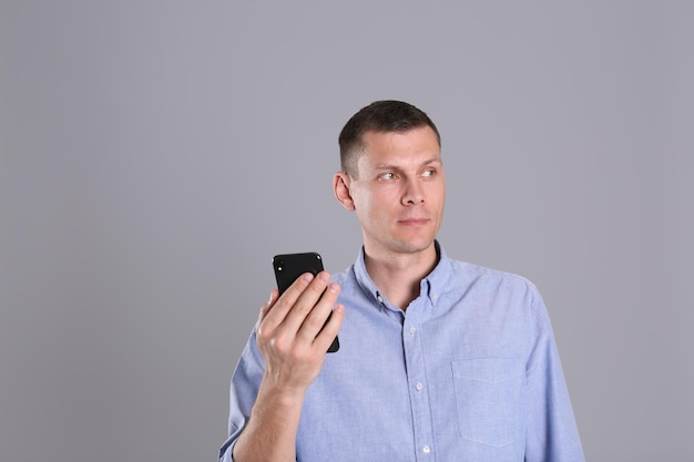 Homme déverrouillant un smartphone avec un scanner facial sur fond gris Vérification biométrique