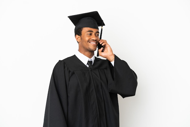 Homme diplômé de l'université afro-américaine sur fond blanc isolé en gardant une conversation avec le téléphone mobile