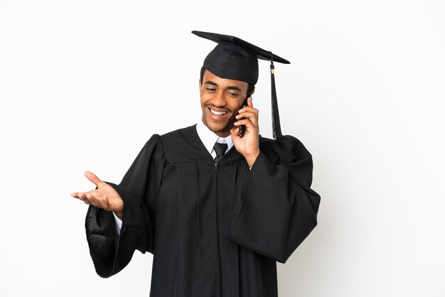 Homme diplômé de l'université afro-américaine sur fond blanc isolé en gardant une conversation avec le téléphone portable avec quelqu'un