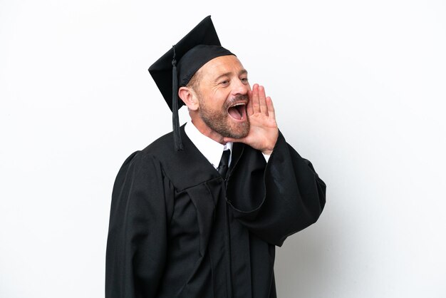 Homme diplômé de l'université d'âge moyen isolé sur fond blanc criant avec la bouche grande ouverte sur le côté