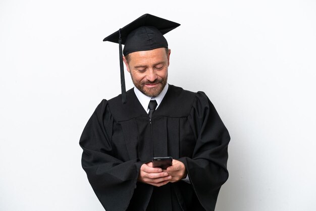 Homme diplômé d'université d'âge moyen isolé sur fond blanc envoyant un message avec le mobile