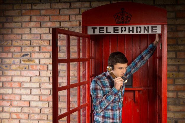 Homme discutant à l'intérieur d'une cabine téléphonique britannique rouge se penchant dans la porte ouverte à l'écoute de la conversation