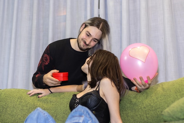 Homme donnant un cadeau à sa petite amie assise sur le canapé Guy donnant un cadeau de la Saint-Valentin à sa petite amie assise sur le canapé