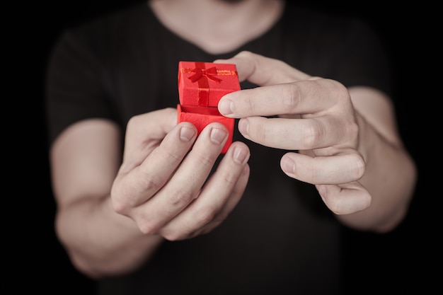 L'homme donne un cadeau dans une boîte cadeau rouge. Cadeau d'ouverture de la Saint-Valentin. Petit coffret cadeau d'anniversaire de l'homme. Petite notion surprise. Fond noir.