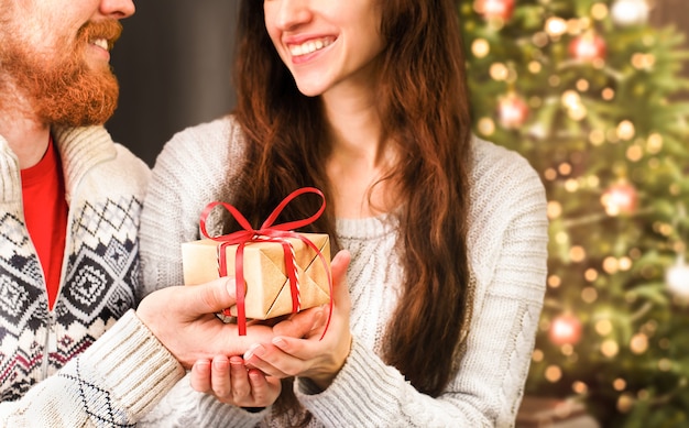 Un homme donne un cadeau de Noël à une femme sur le fond d'un arbre de Noël